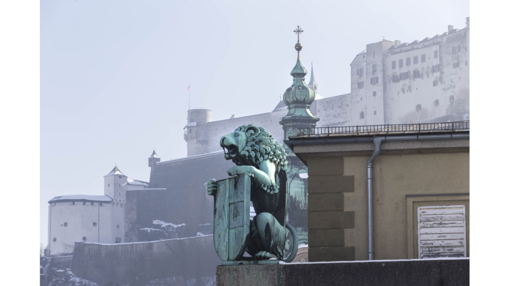 Eine Löwenstatue, im Hintergrund ist der Salzburger Dom zu erkennen