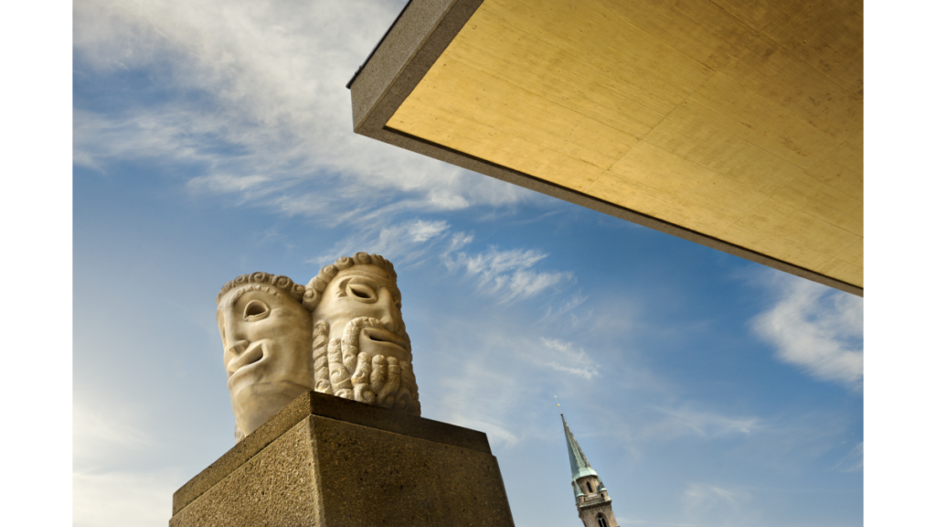 Eine Statue mit zwei Schauspielmasken vor dem Salzburger Festspielhaus