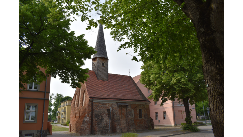 Die kleine Sankt Georg Kapelle in Neuruppin, diesemal von der Südseite zwischen Bäumen