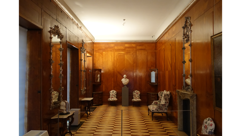 Ein mit Zedernholz vertäfelter Raum mit an den Wänden verteilten Sesseln und Skulpturen