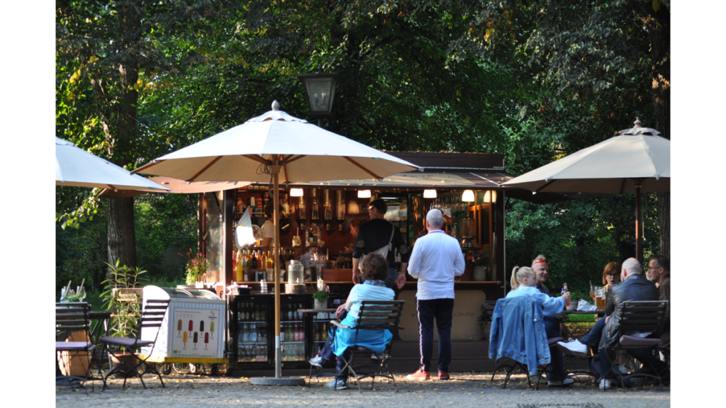 Ein Café am Eingang des Schlossparks. Gäste sitzen unter Sonnenschirmen