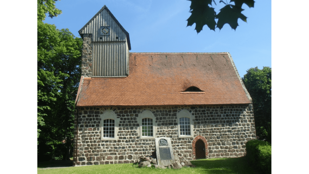 Eine kleine steinerne Dorfkirche mit rotem Dach und einen kleinen Turm mit Uhr