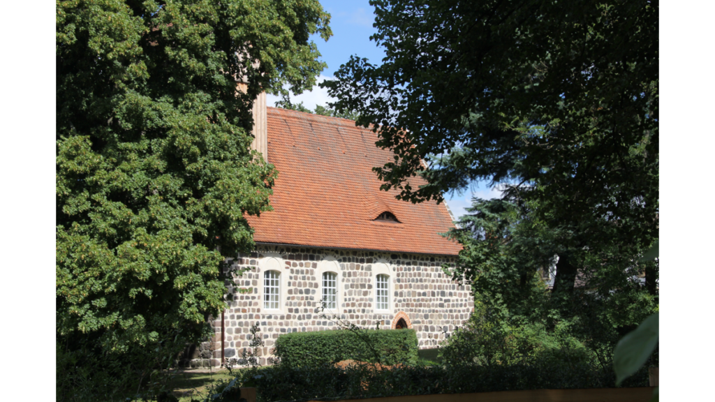 Die steinerne Seitenwand einer Kirche mit rotem Dach, eingerahmt von Bäumen
