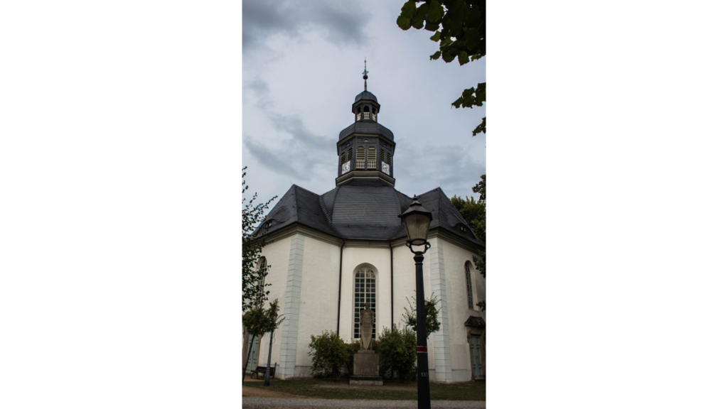 Eine weiß gehaltene Kirche mit einem kleinen Glockenturm. Das Dach ist aus grauem Schiefer