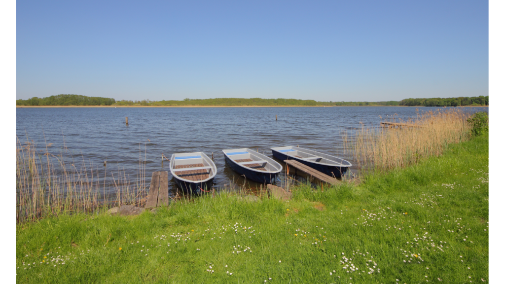 Drei Ruderboote liegen an einem kleinen Steg an einem See