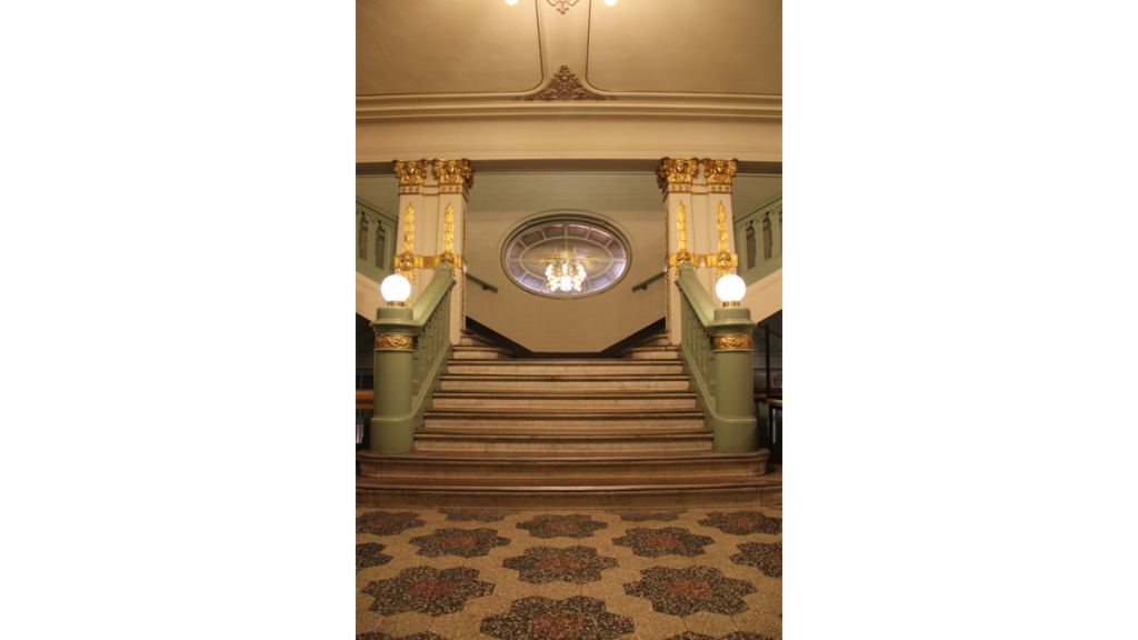 Eine prächtige, goldverzierte Treppe im Rathaus Pankow mit zwei Lampen, die sich teilt