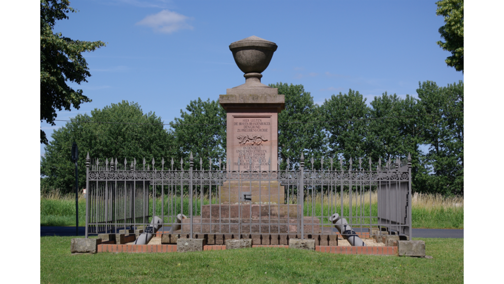 Ein mit einem eisernen Zaun abgetrenntes Denkmal, einer großen gusseisernen Schale