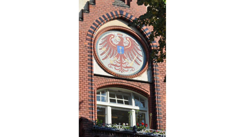 Ein rundes Medaillon mit dem roten brandenburgischen Adler in einem Fensterbogen am Rathaus Lichtenberg
