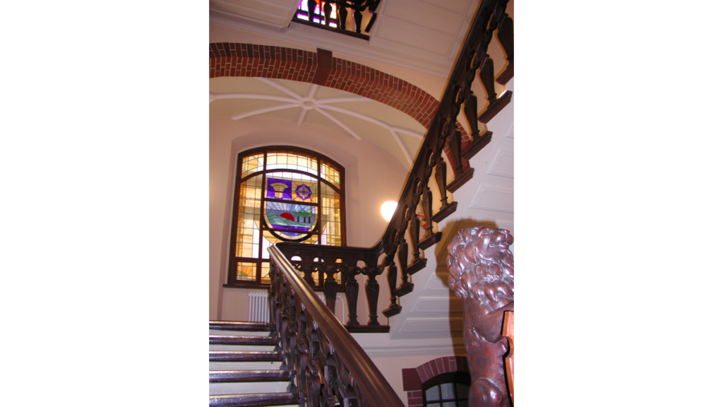 Eine zweistufige Treppe mit einem Holzgeländer und einem Buntglasfenster