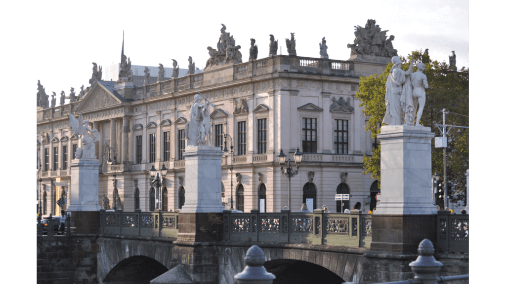 Eine Brücke mit steinernen Statuen auf jeder Seite, dahinter ein klassisches Gebäude
