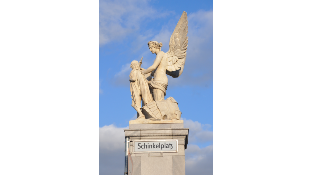 Eine Statue einer geflügelten Göttin mit einem nackten Knaben, sie heißt "Nike lehrt dem Knaben Heldensagen"
