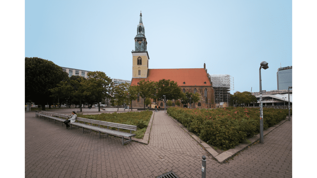 Der Blick von einem Park aus auf die St.Marienkirche. Sie besitzt ein rot gedecktes Dach und einen kleinen Glockenturm mit Spitze.