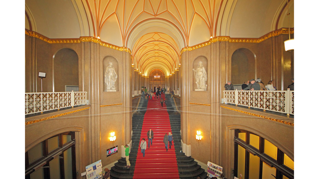 Eine lange Treppe mit rotem Läufer, die in den 2.Stock eines großen klassischen Rathauses führt