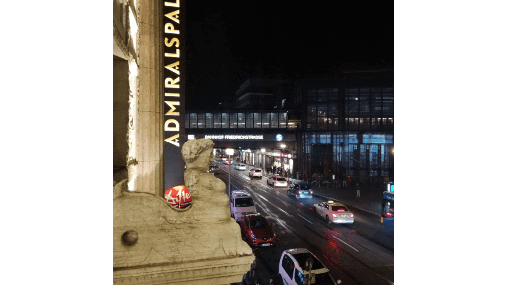 Der Blick aus einem Gebäude, dem Admiralspalast, auf eine nächtliche Straße, die zum Bahnhof Friedrichstrasse führt