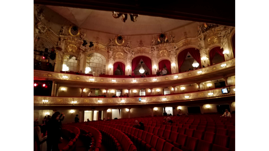 Der runde Zuschauersaal in der Komischen Oper. Die Wände sind im klassischen Stil gehalten, die Sitze sind rot