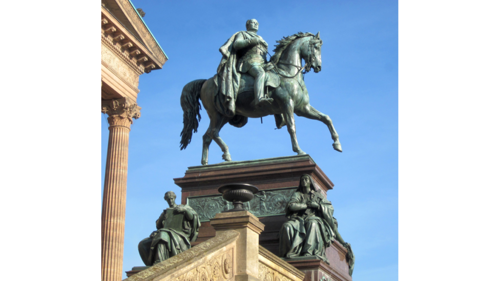 Eine Detailansicht des Reiterstandbilds von Friedrich Wilhelm IV.. Unter dem Reiter befinden sich zwei allegorrische Frauenfiguren.