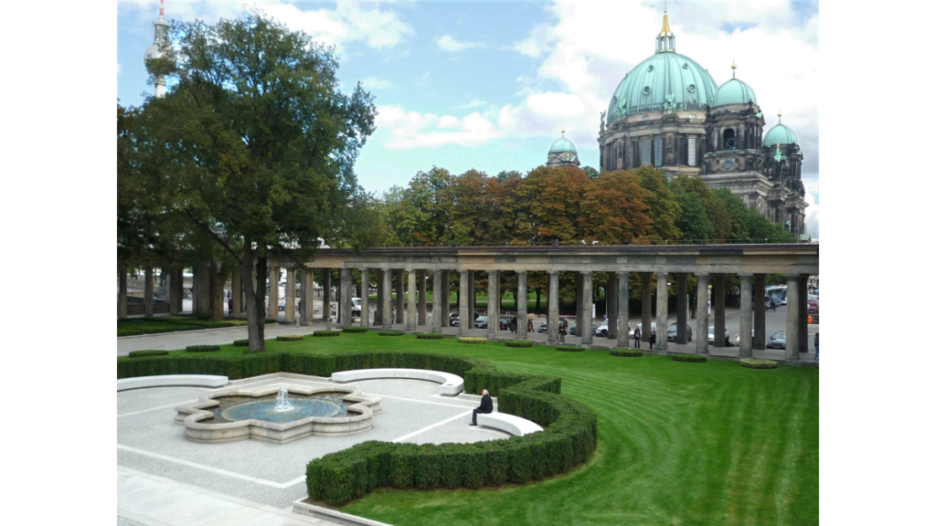 Der Kolonnadenhof der Alten Nationalgalerie mit einem Springbrunnen und dem Säulengang. Im Hintergrund ist der Berliner Dom zu sehen.