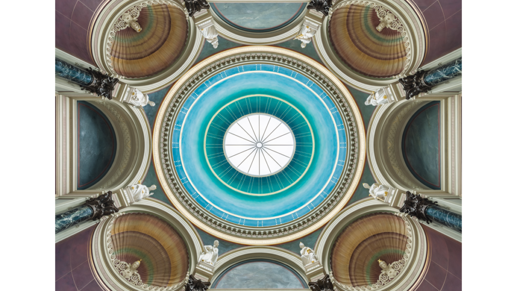 Der Blick von unter direkt hinauf in die blaue Kuppel der Alten Nationalgalerie. Um die Kuppel herum befinden sich Rotunden mit Büsten, die von Statuen eingefasst werden