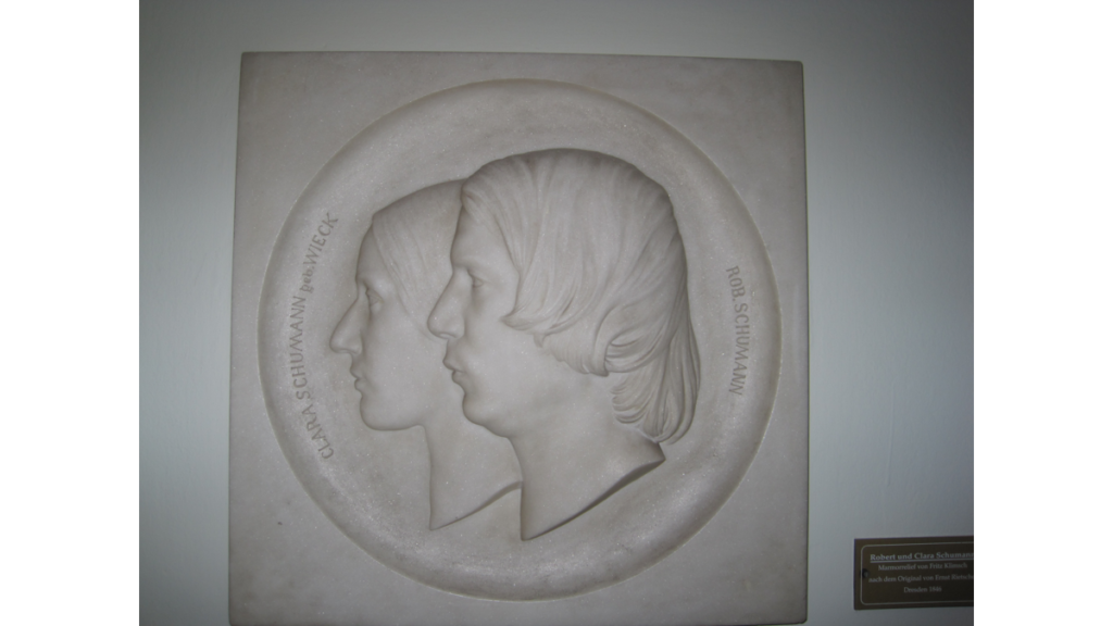 Ein als Medaillon angelegtes Doppelporträt von Clara Schumann und Robert Schumann. Es zeigt beide Gesichter von der Seite