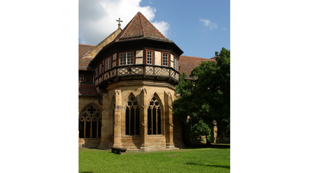 Ein zweistöckiges, fast rundes Brunnenhaus im Kloster Maulbronn mit Bogenfenstern unten und einen Fachwerkaufsatz mit spitzem Dach oben