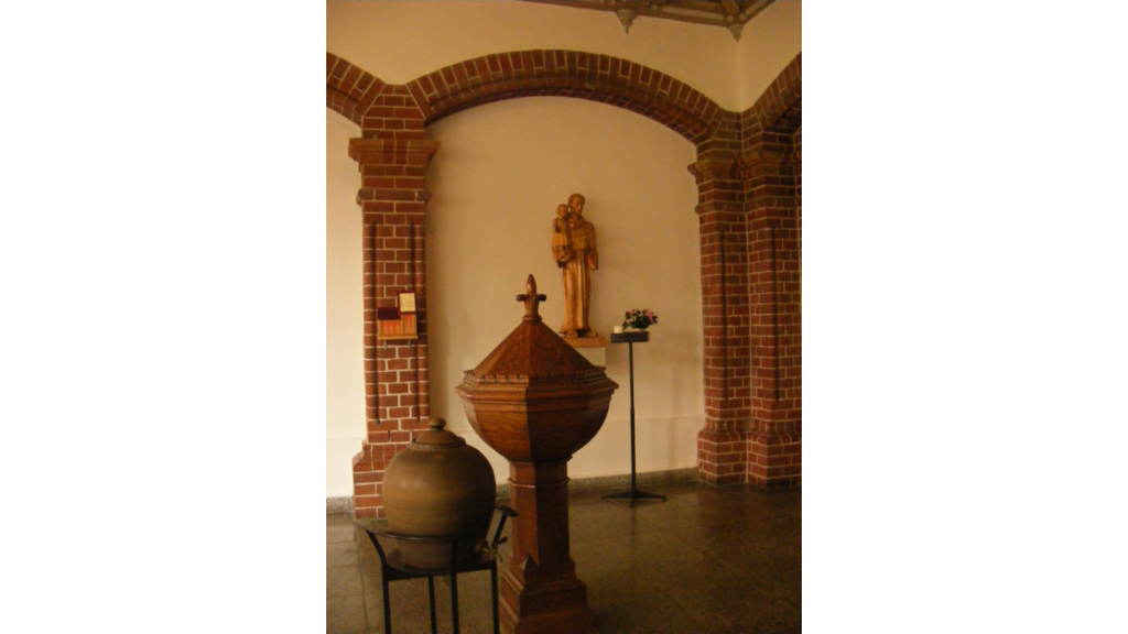 Das Taufbecken in der Sankt Georg-Kirche, dahinter eine Figur des barmherzigen Samariters