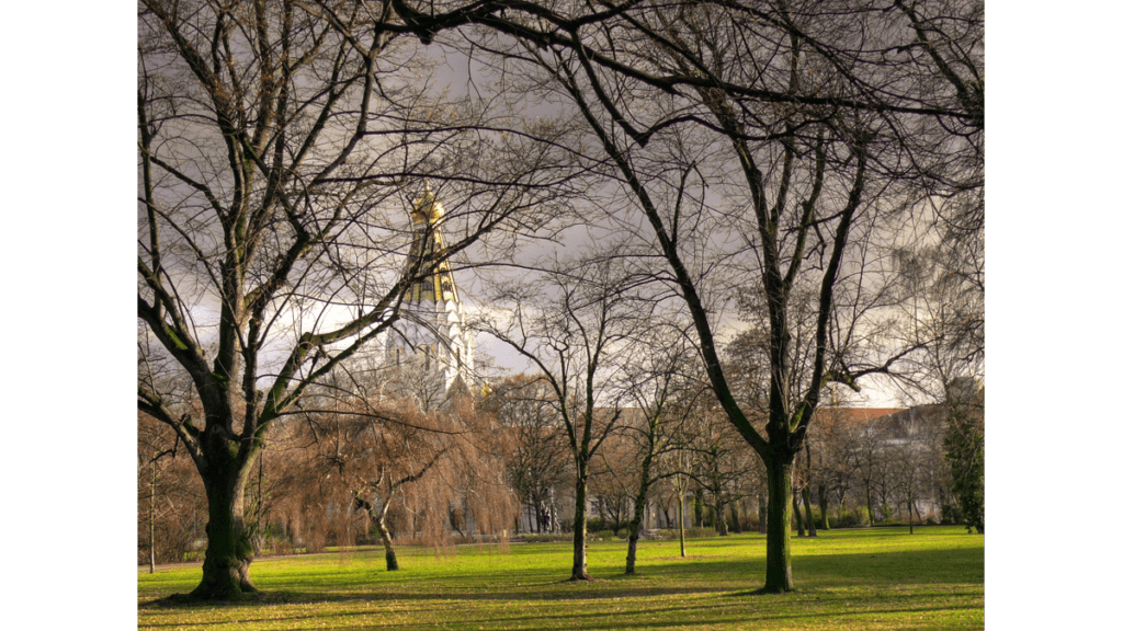 Weitläufiges Gelände des Friedensparks in Leipzig. Durch die Bäume schimmert die russische Gedächtniskirche von 1913