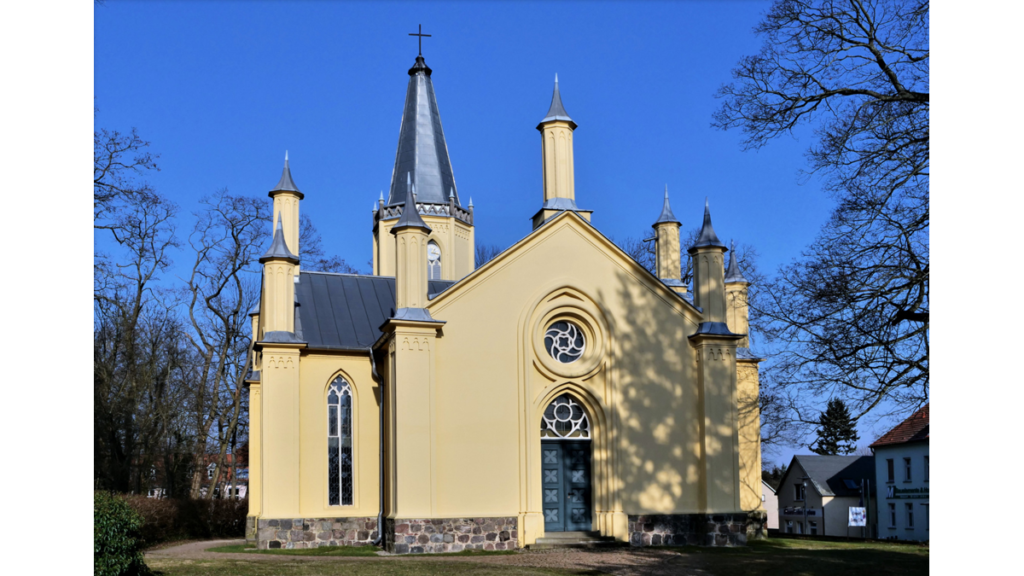 Die ockerfrabene Schinkelkirche mit dem kleinen Glockenturm und den kleineren Türmchen am Kirchenschiff