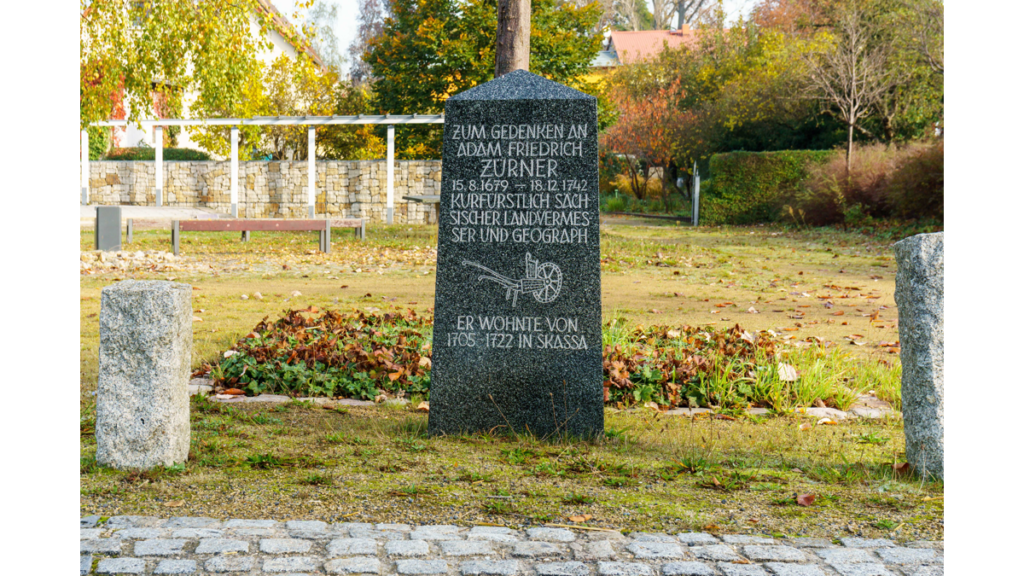 Ein Denkmal in Skassa in Erinnerung an Zürner, auf dem steht: "Zum Gedenken an Adam Friedrich Zürner. 15.8.1679-18.12.1742. Kurfürstlich sächsischer Landvermesser und Geograph. Er wohnte von 1705-1722 in Skassa."