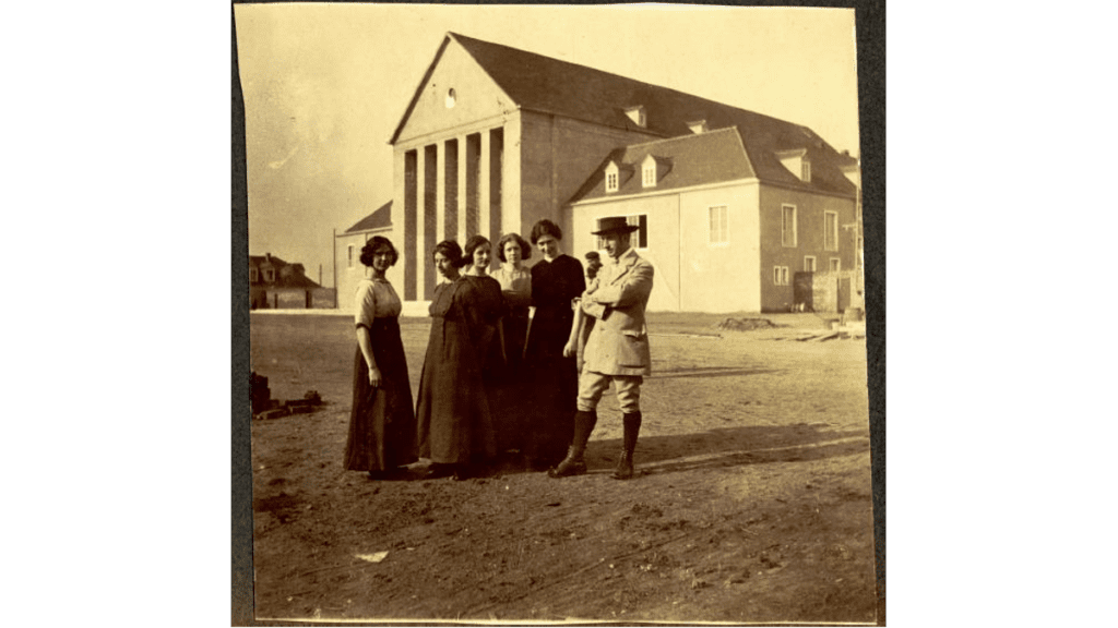 Eine schwarz-weiß Fotografie von Emile Jaques-Dalcroze mit seinen Schülerinnen vor dem neu gebauten Festspielhaus in der Gartenstadt Hellerau.