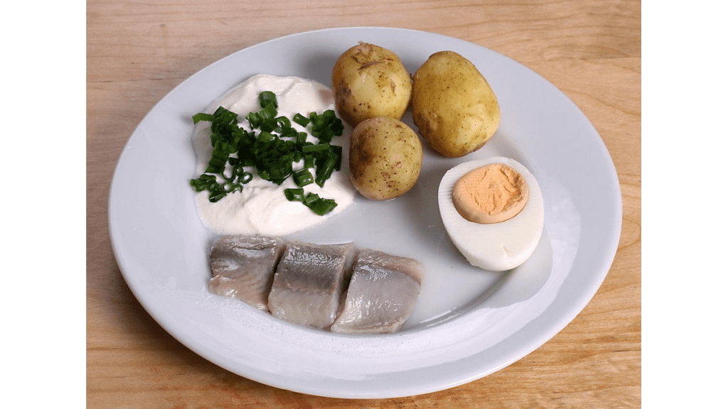 Ein Teller mit einem Bismarck-Hering, Kartoffeln, Ei und Sauerrahm.