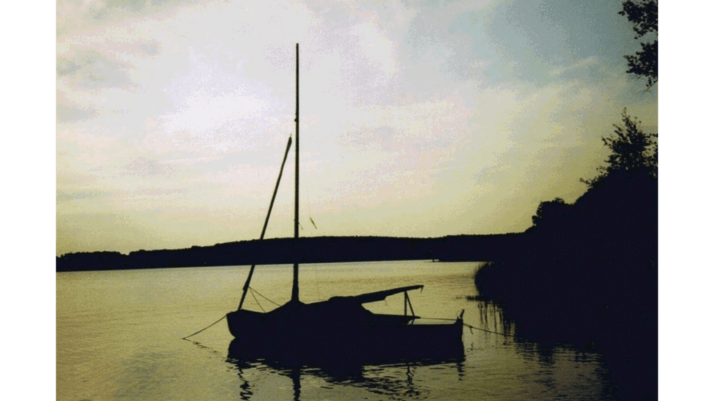 Ein kleines Segelboot ankert bei Sonnenuntergang auf dem Möserschen See, einer der drei goldenen Seen.
