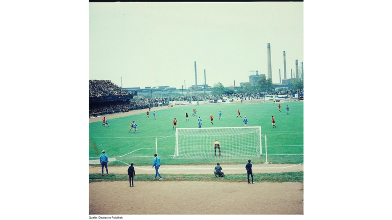Hier kickt der Fußballverein Stahl Riesa im Jahr 1983 im heute nicht mehr genutzten Ernst-Grube-Stadion vor einer Kulisse aus Industrieschloten.