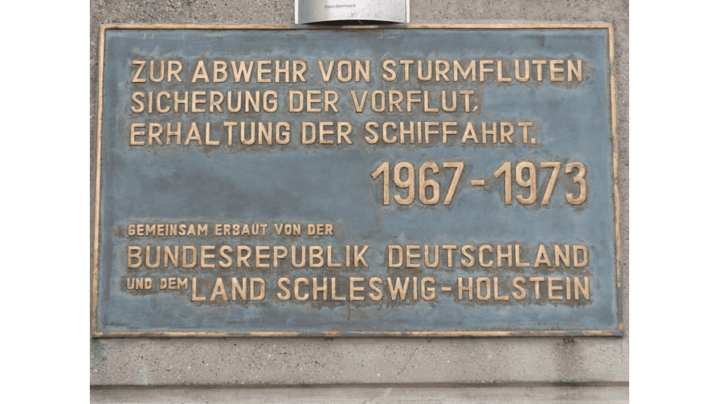Eine Erinnerungsplakette an den Bau des Eidersperrwerks. Dort steht: Zur Abwehr von Sturmfluten, Sicherung der Vorflut, Erhaltung der Schiffahrt. 1967 - 1973.