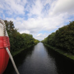 Der Blick von einer Brücke auf einen Kanal. Links hängt ein rot-weißer Rettungsring