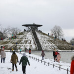 Vor dem winterlichen Hügel des Otto Lilienthal-Denkmals tummeln sich viele Eingemummelte, die rodeln oder spazieren gehen