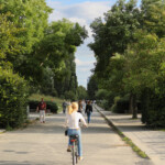 An einem langen Weg inmitten des grünen Mauerparks flanieren Menschen oder fahren Rad
